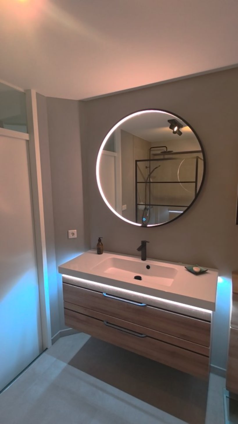 Badkamer met wanden in betonlook en een ronde verlichte spiegel