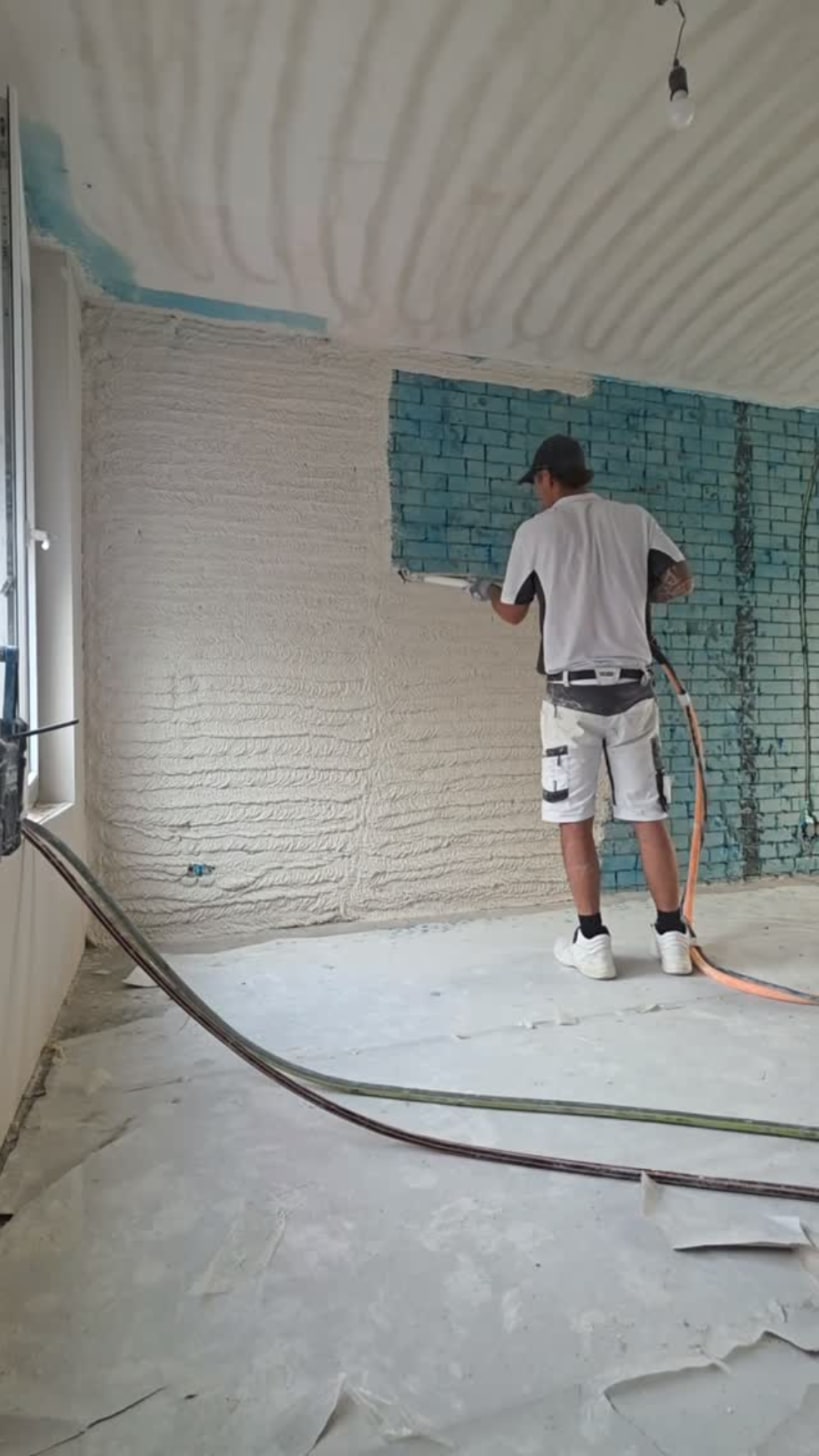 Stukadoor spuit gips met de machine op een wand, een deel van de muur en het plafond zit er al op