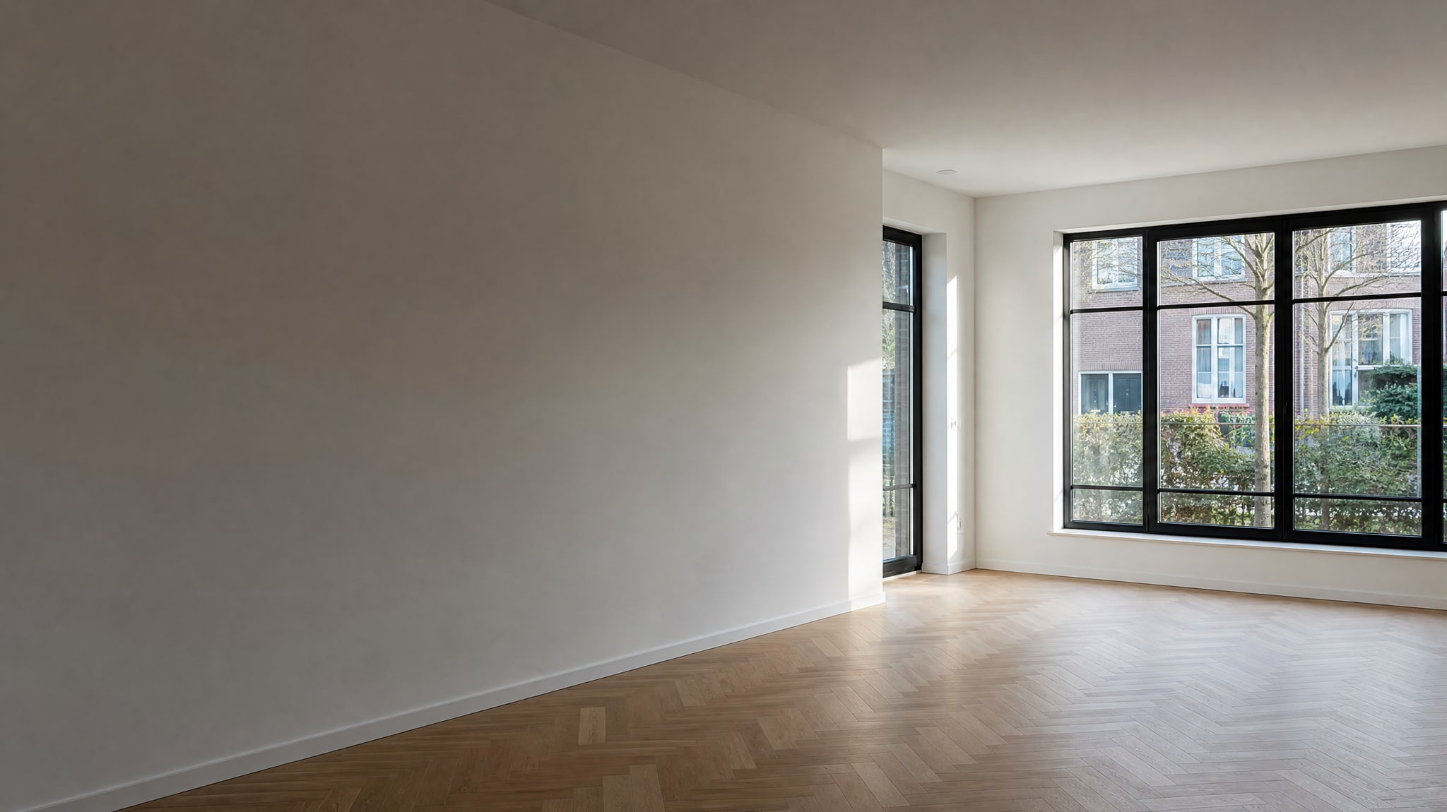 Lege woonkamer met strak gestucte witte wanden en plafond, daglicht strijkt langs de wand