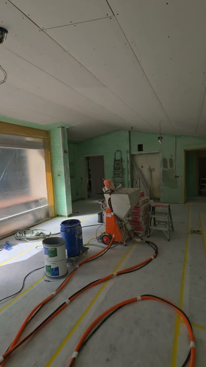 Stucmachine met slangen in een woonkamer die klaarstaat om gestuct te worden