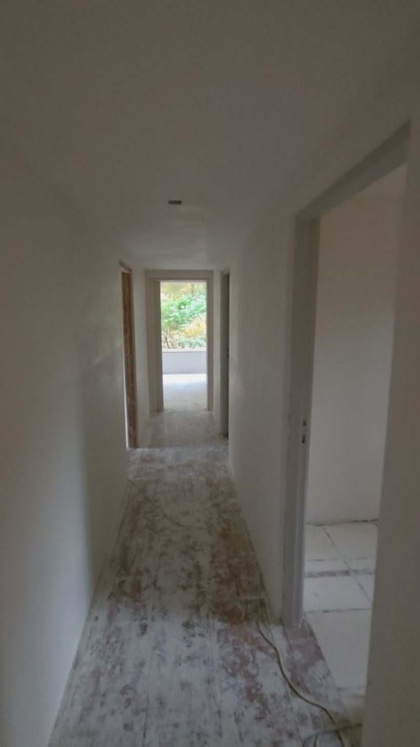 Lange gang met glad gestucte wanden en plafond, met aan het eind uitzicht op groen