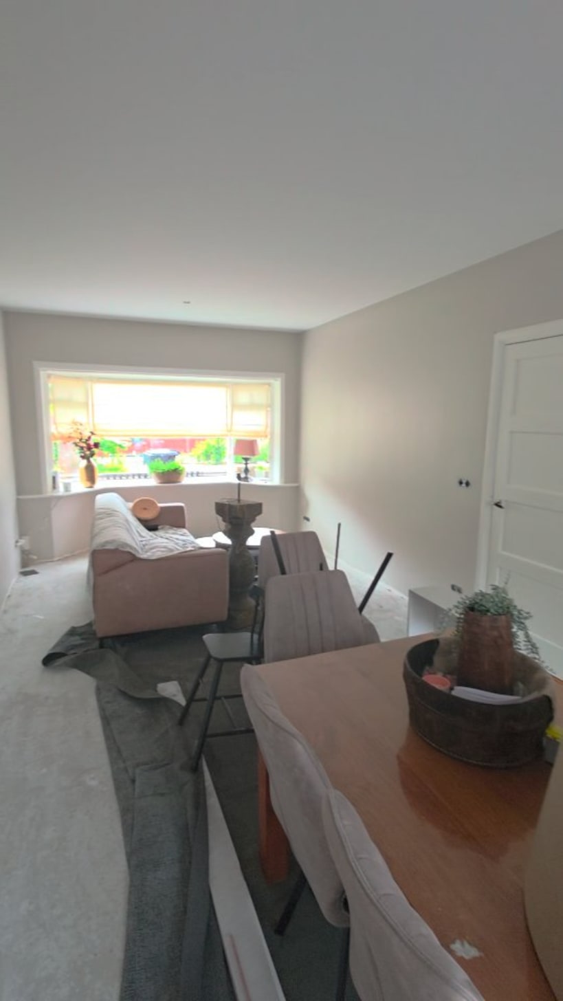 Woonkamer met lichte wanden en een strak plafond, de meubels staan nog in het midden