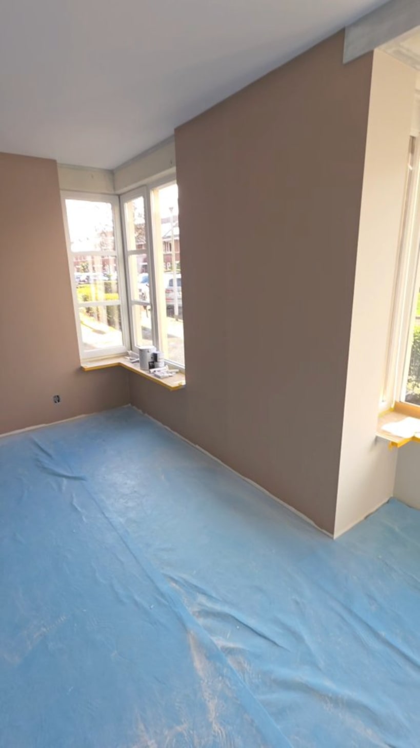 Kamer met wanden in een warme taupe kleur en witte kozijnen, de vloer is nog afgedekt